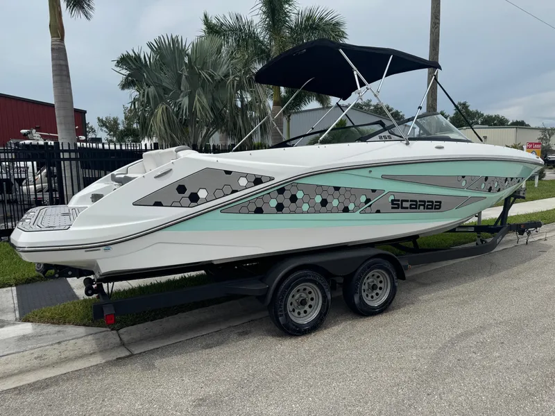 Slide: The Image of 2020 Scarab 255 Open ID boat on trailer, parked near palm trees. - 3