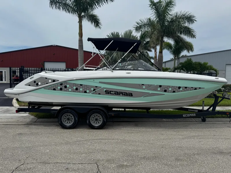 Slide: The Image of 2020 Scarab 255 Open ID boat on trailer, parked near palm trees and industrial buildings. - 5