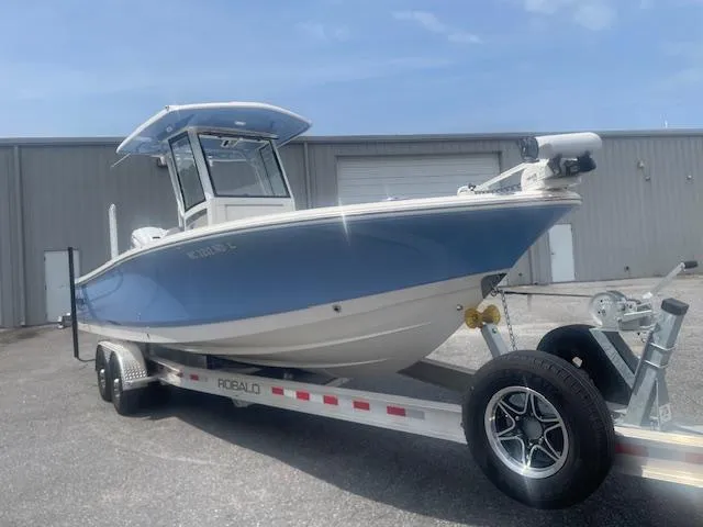 Slide: The Image of 2023 Robalo 266 Cayman boat on trailer, parked outdoors near a warehouse. - 2