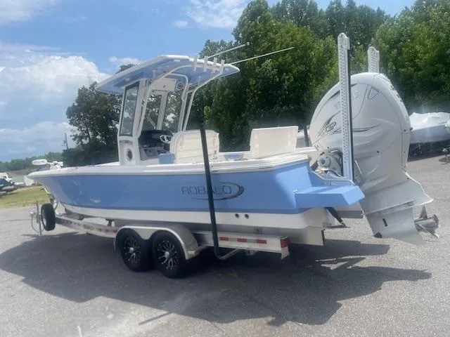 Slide: The Image of 2023 Robalo 266 Cayman boat on trailer, light blue hull, dual engines, parked outdoors. - 4