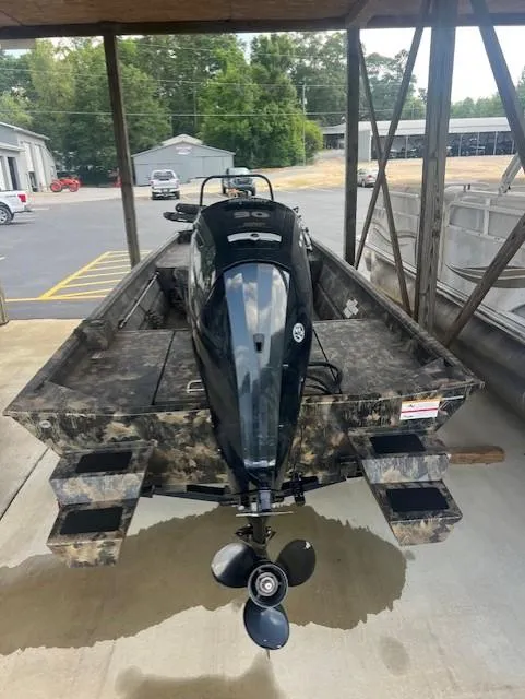 Slide: The Image of 2023 Lowe Roughneck 1860 CC boat with camouflage design and outboard motor, parked under shelter. - 4
