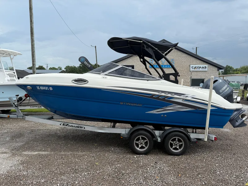 The Image of 2018 Stingray 214 LR boat on trailer, blue and white design, parked outdoors. - 1