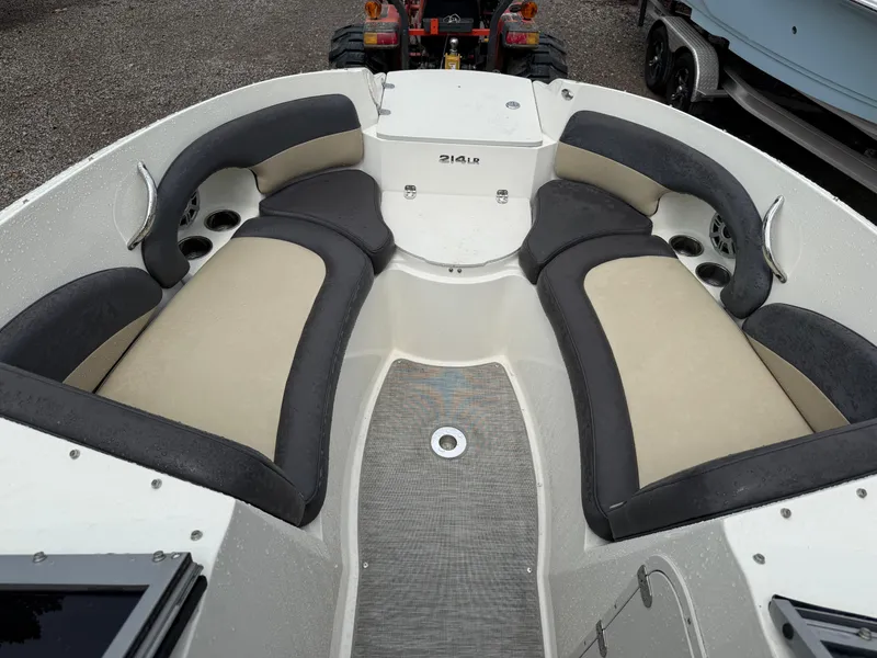 Slide: The Image of 2018 Stingray 214 LR boat interior with beige and black seating, cup holders, and textured flooring. - 13