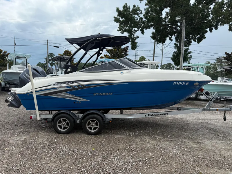 Slide: The Image of 2018 Stingray 214 LR boat on trailer, blue and white design, parked outdoors. - 8