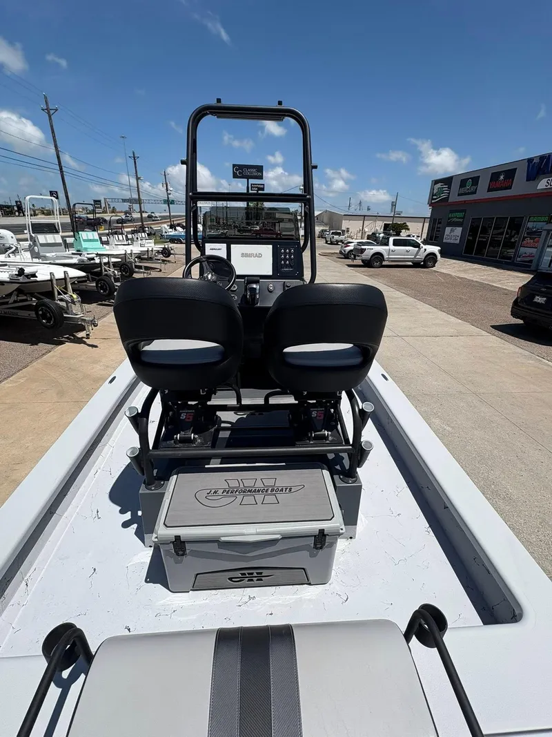 Slide: The Image of 2022 JH Performance Outlaw 250 boat interior with dual seats and console, parked outdoors. - 13
