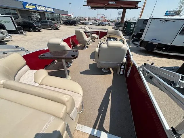 Slide: The Image of 2012 Bennington R25 pontoon boat interior with beige seating and red accents at a marine center. - 18