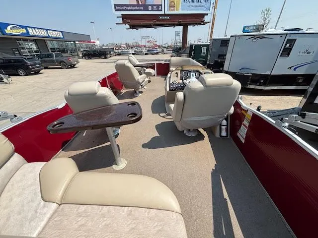 Slide: The Image of 2012 Bennington R25 pontoon boat interior with beige seating and table, parked at a marine center. - 19