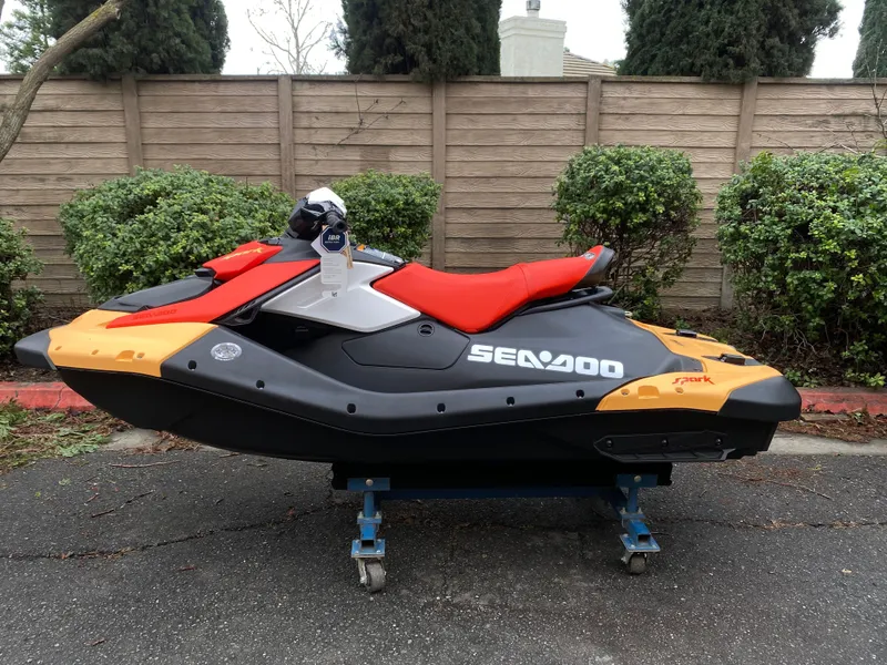 The Image of 2024 Sea-Doo Spark 2up jet ski with vibrant red and orange design, parked outdoors. - 1