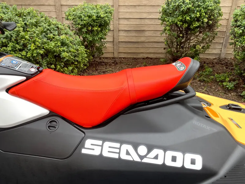 Slide: The Image of 2024 Sea-Doo Spark 2up with vibrant red seat, parked near green bushes. - 3