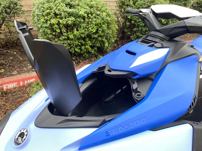 Slide: The Image of 2024 Sea-Doo Spark 3up in blue, open storage compartment, parked near greenery. - 3