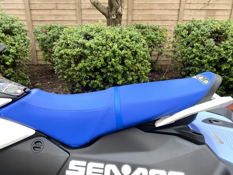 Slide: The Image of 2024 Sea-Doo Spark 3up with blue seat, parked near green bushes. - 5