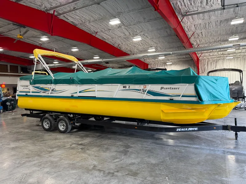Slide: The Image of 2004 PlayCraft 2800 Powertoon boat with yellow hull, covered, on trailer in warehouse. - 15
