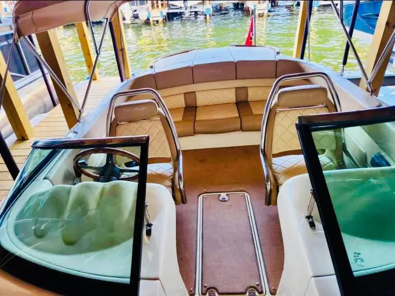 Slide: The Image of 2016 Chris-Craft Carina 21 boat interior with tan seating and steering wheel, docked by water. - 5