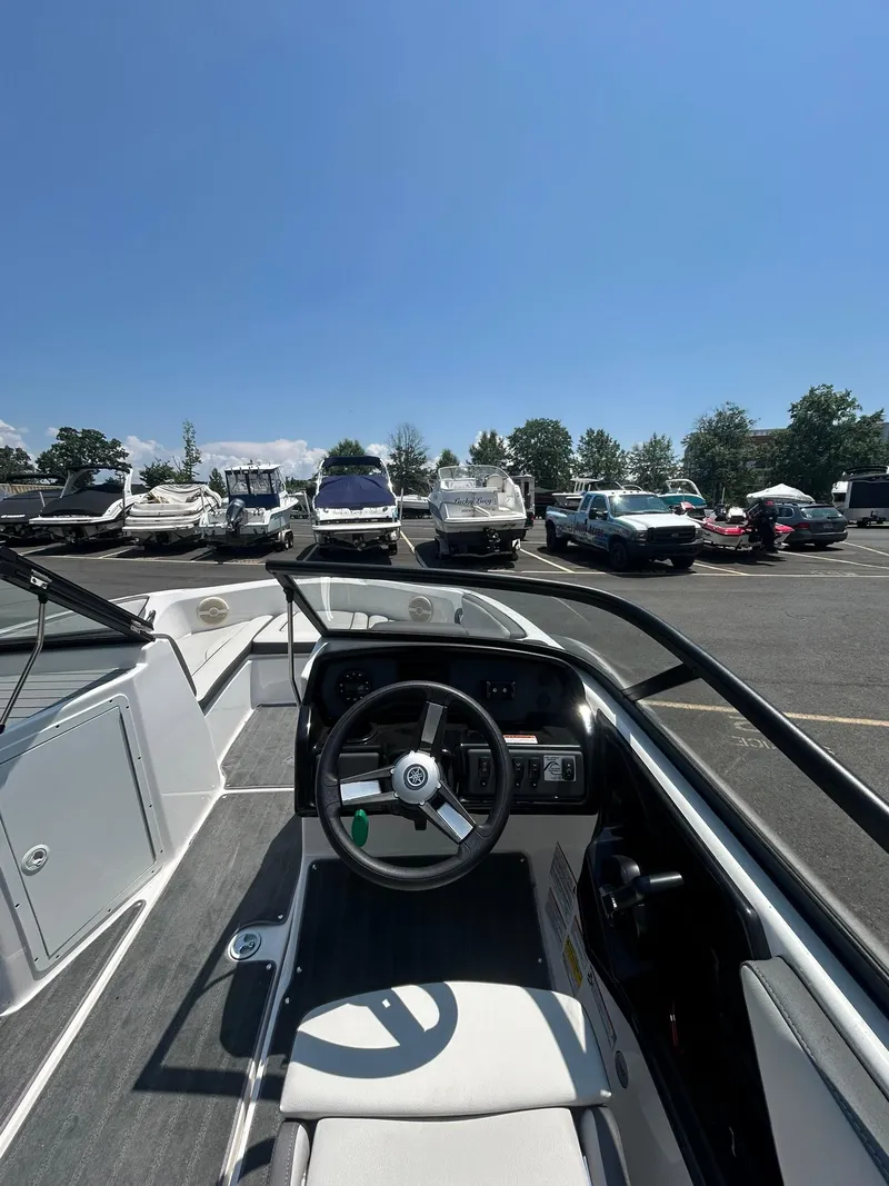 Slide: The Image of 2024 Yamaha Boats SX190 interior with steering wheel, parked among other boats and vehicles. - 10