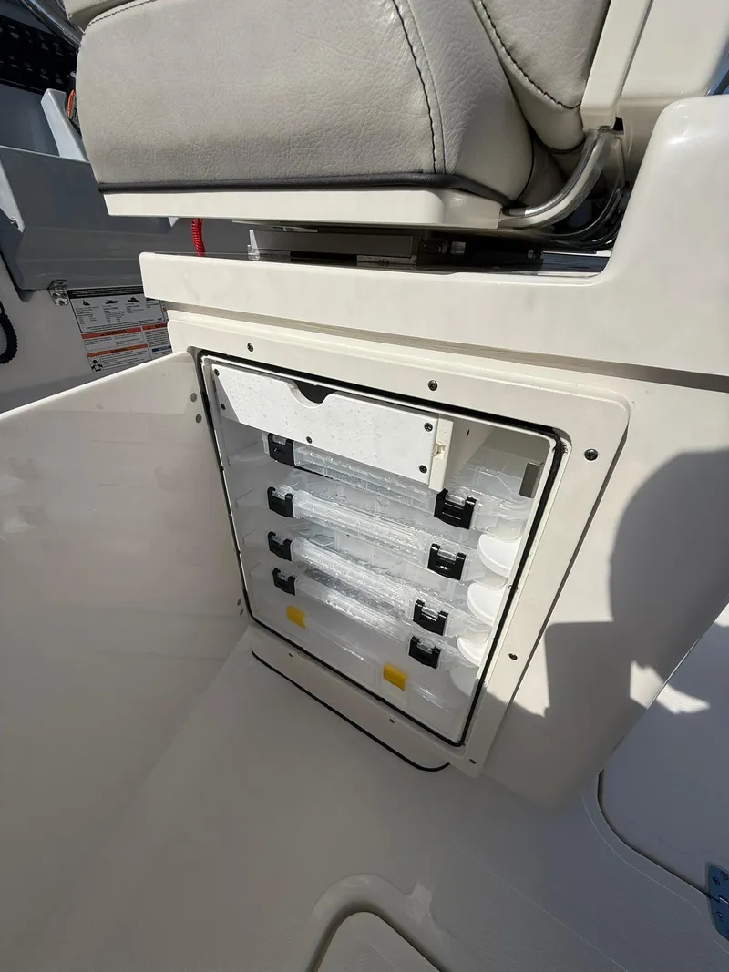 Slide: The Image of 2023 Pursuit S 268 Sport boat storage compartment with tackle trays and cushioned seat. - 24