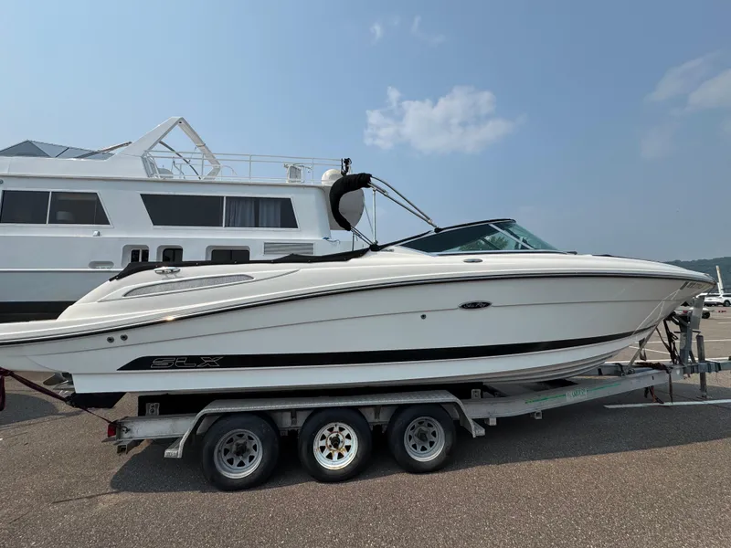 Slide: The Image of 2012 Sea Ray 270 SLX boat on trailer, parked near a larger vessel, under clear skies. - 2