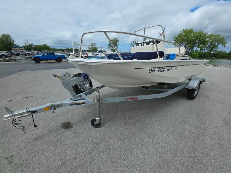 Slide: The Image of 2024 Boston Whaler 150 Montauk on trailer, parked outdoors under cloudy sky. - 2
