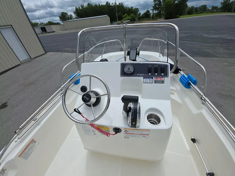 Slide: The Image of 2024 Boston Whaler 150 Montauk boat console with steering wheel and controls, parked outdoors. - 9