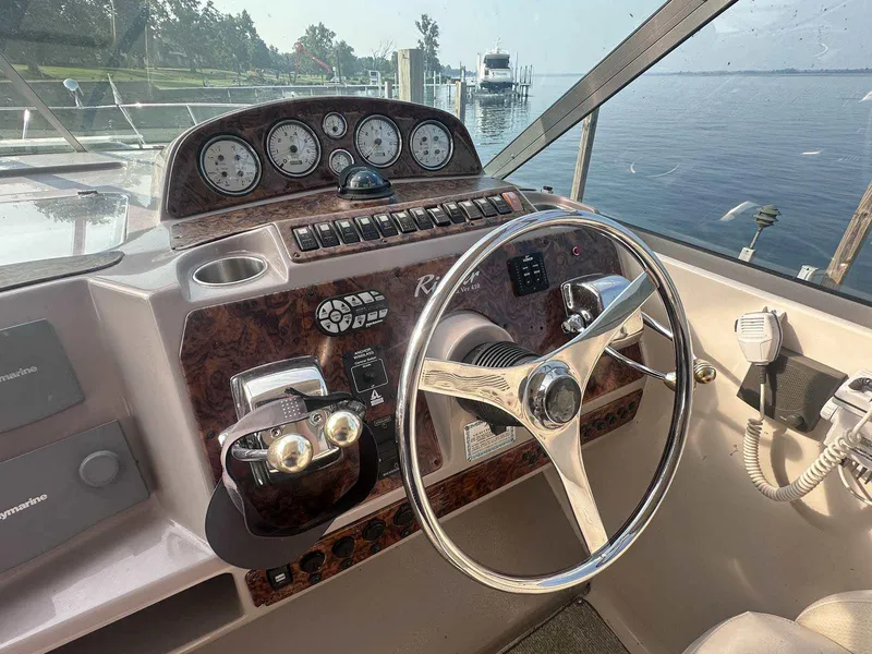 Slide: The Image of 2004 Rinker Fiesta Vee 410 helm with gauges, steering wheel, and controls, overlooking a serene lake. - 8