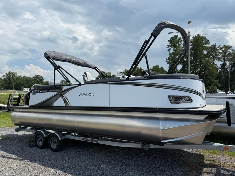 Slide: The Image of 2025 Avalon LSZ Quad Lounger Shift pontoon boat on trailer, parked outdoors. - 2