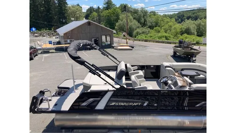 Slide: The Image of 2025 Starcraft EXS 1 Q DH pontoon boat in parking lot, surrounded by trees. - 2