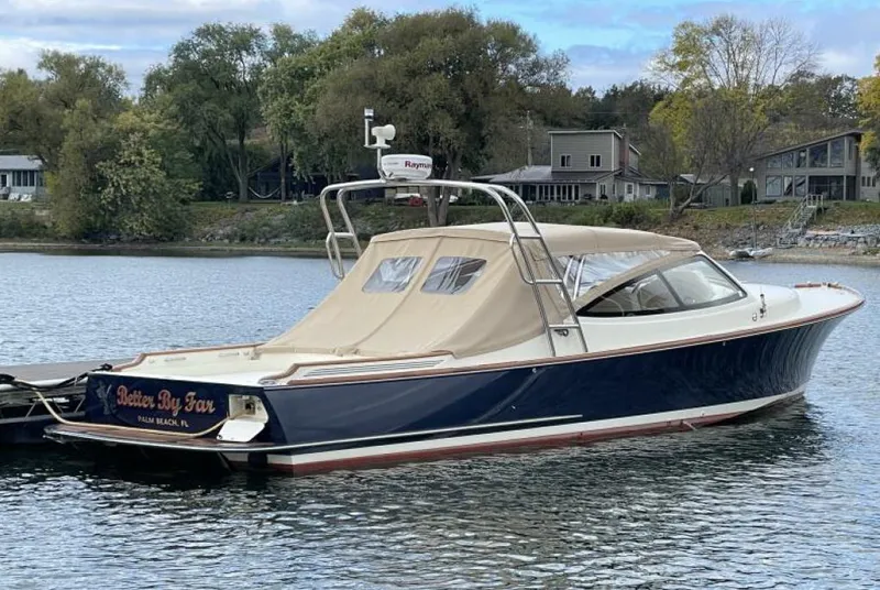 Slide: The Image of 2012 Hinckley Talaria boat docked on a serene lake with surrounding trees and houses. - 0