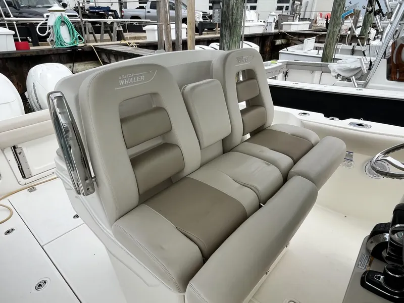 Slide: The Image of 2018 Boston Whaler 330 Outrage boat seating, featuring plush, beige upholstery at a marina. - 18