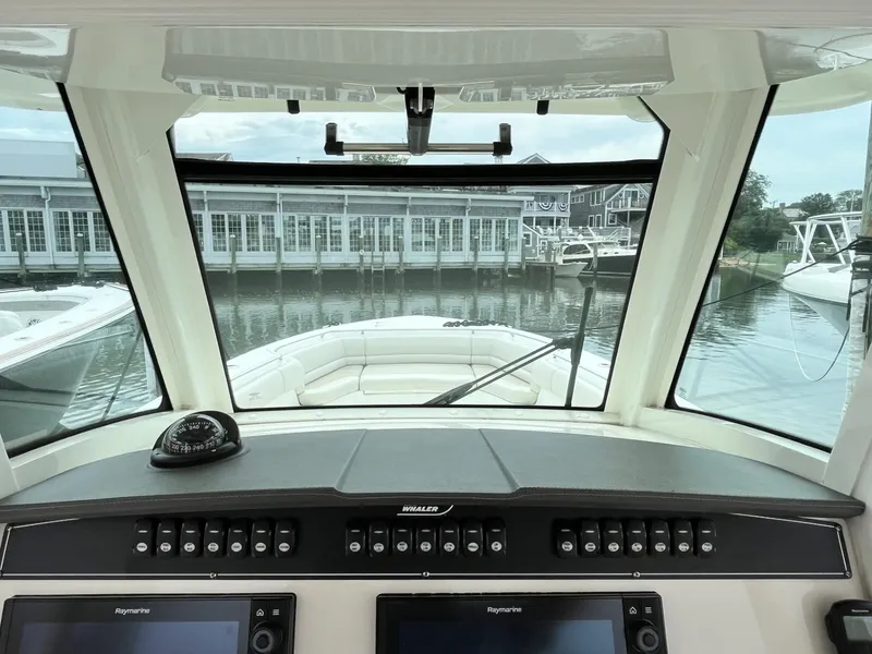 Slide: The Image of 2018 Boston Whaler 330 Outrage helm view with marina backdrop. - 22