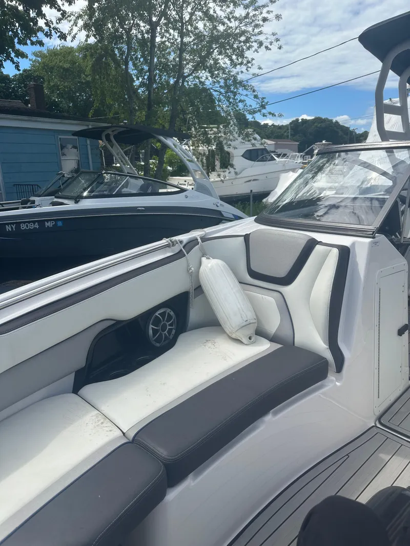 Slide: The Image of 2021 Yamaha Boats 252S interior with white seating and speaker, docked near other boats. - 11