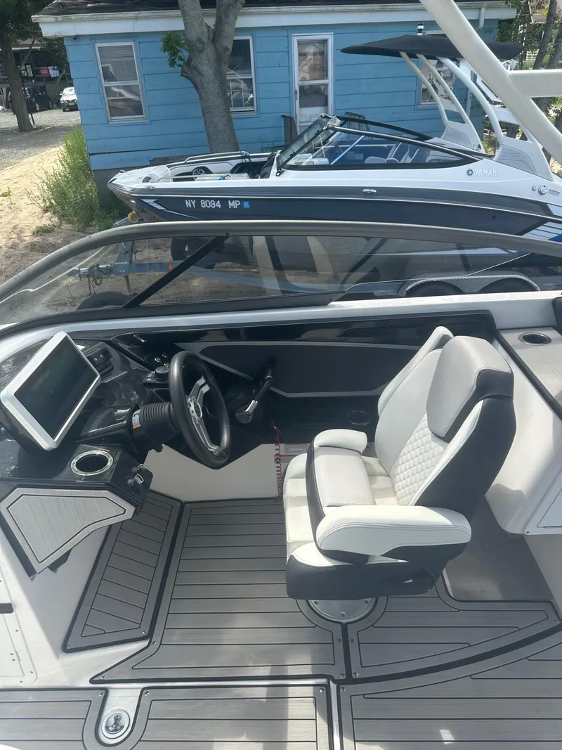 Slide: The Image of 2021 Yamaha Boats 252S interior with steering wheel and seating, docked near a blue house. - 18