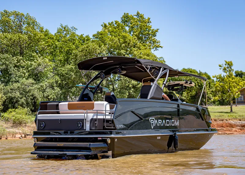 Slide: The Image of 2025 Paradigm 236 boat on water, sleek design, black canopy, lush green background. - 3
