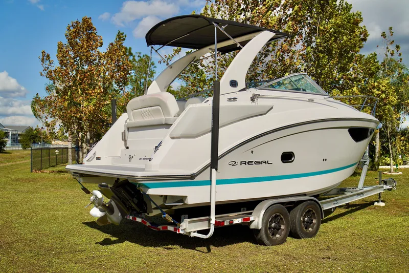 Slide: The Image of 2019 Regal 26 Express boat on trailer, parked on grass with trees in background. - 8