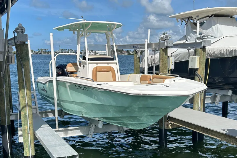 Slide: The Image of 2023 NauticStar 231 Hybrid boat on lift, docked by the water under a clear blue sky. - 2