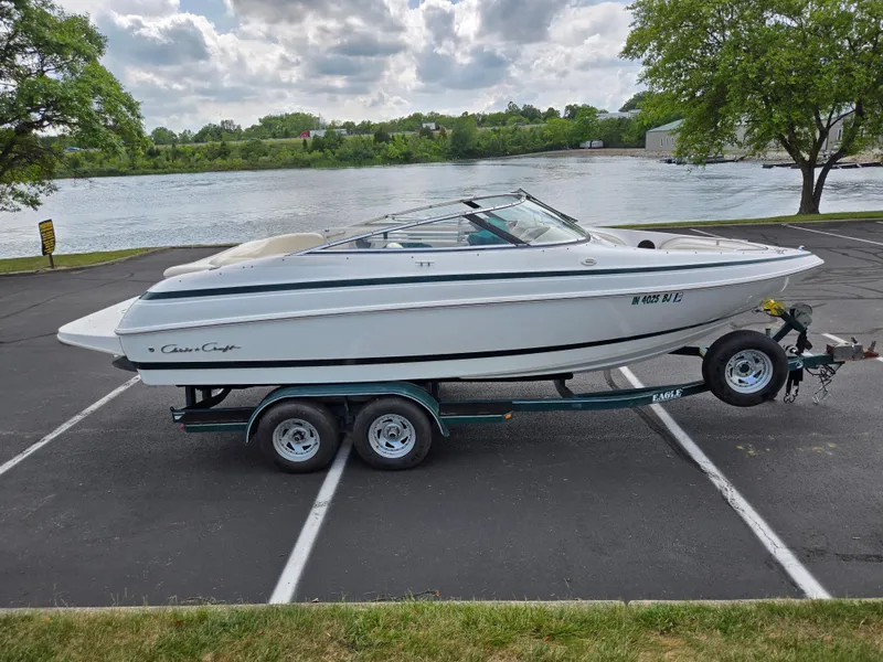 Slide: The Image of 1998 Chris-Craft 210 Bowrider boat on trailer by a lake under clear blue sky. - 9