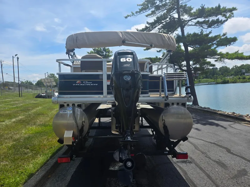 Slide: The Image of 2023 Sun Tracker Bass Buggy 18 DLX pontoon boat with 60 HP engine by a lake. - 2