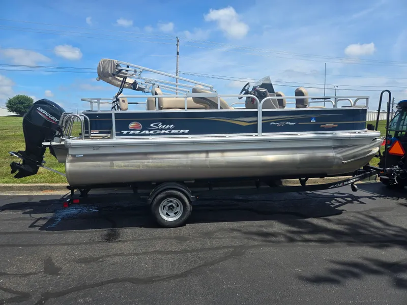 Slide: The Image of 2023 Sun Tracker Bass Buggy 18 DLX pontoon boat on trailer, parked outdoors. - 4