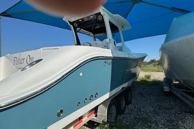 Slide: The Image of 2023 Edgewater 370CC boat under blue canopy, parked on gravel. - 17