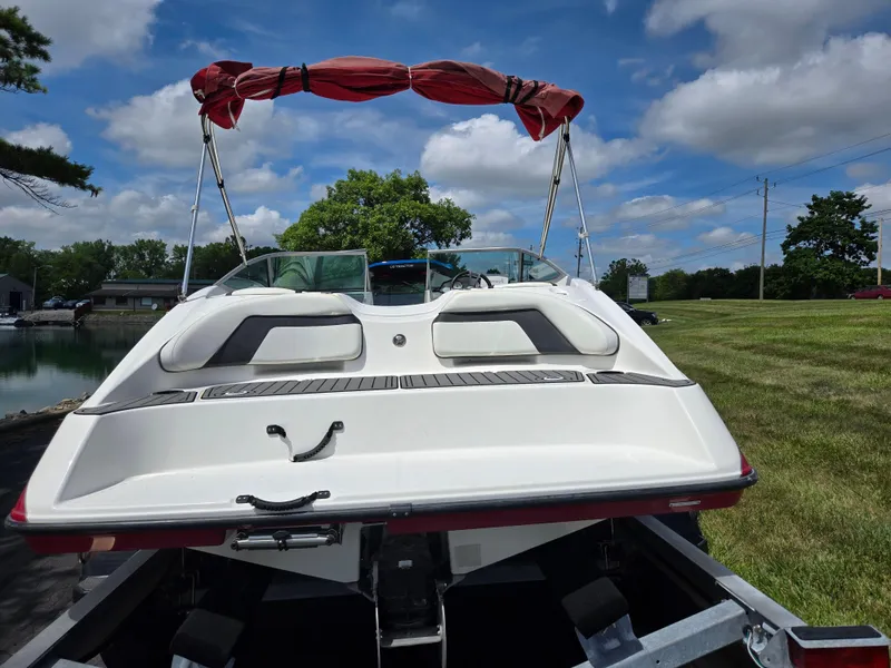 Slide: The Image of 2015 Yamaha Boats SX190 on trailer, red canopy, parked near water and grassy area. - 2