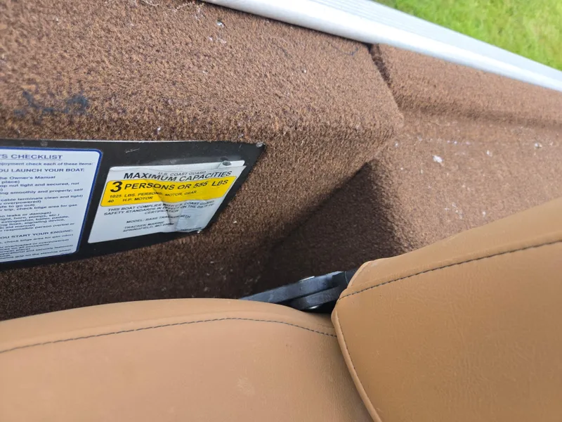 Slide: The Image of 2018 Tracker Bass Tracker boat interior with capacity label, brown upholstery, and tan seat. - 13