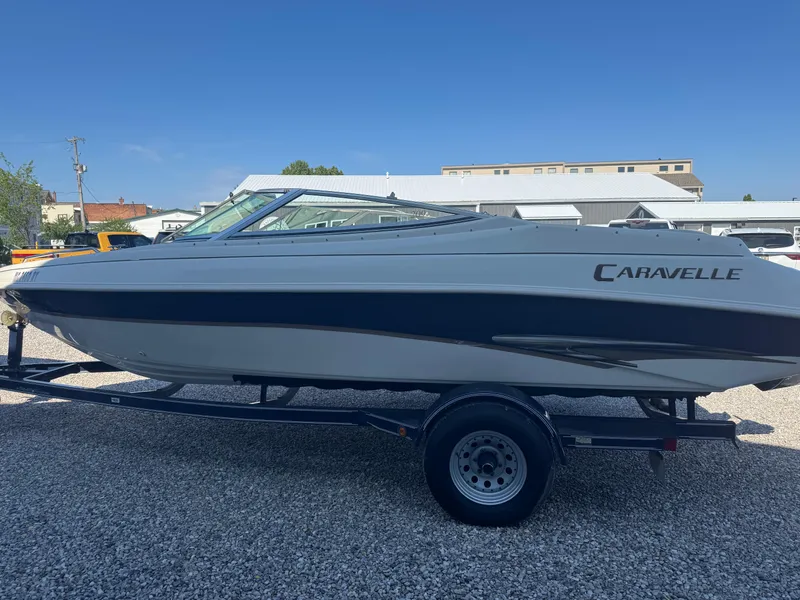Slide: The Image of 1999 Caravelle 209 Bow Rider boat on trailer, parked on gravel, under clear blue sky. - 4