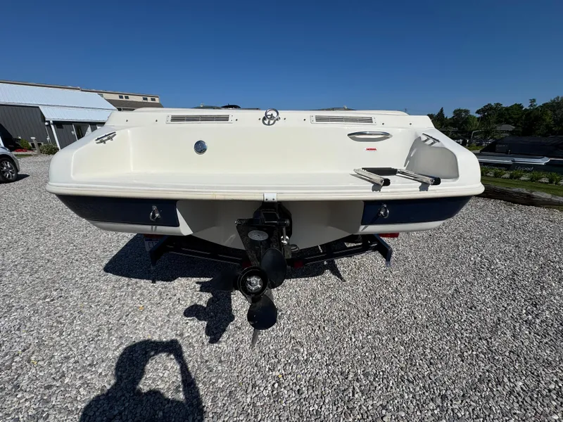 Slide: The Image of 1999 Caravelle 209 Bow Rider boat, rear view on gravel, showcasing propeller and swim platform. - 8