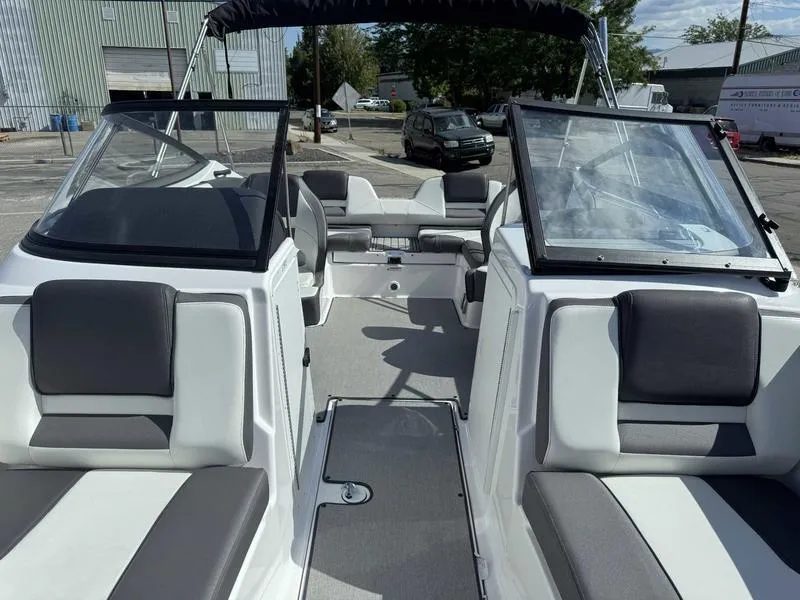 Slide: The Image of 2022 Yamaha Boats SX210 interior with gray seating and open windshield, parked outdoors. - 9