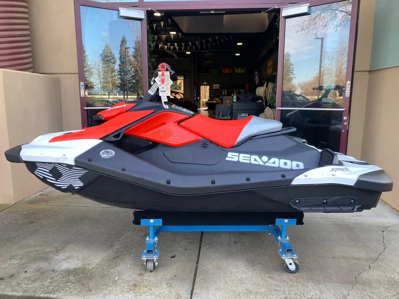 The Image of 2024 Sea-Doo Spark Trixx jet ski in red and black, displayed on a stand. - 0