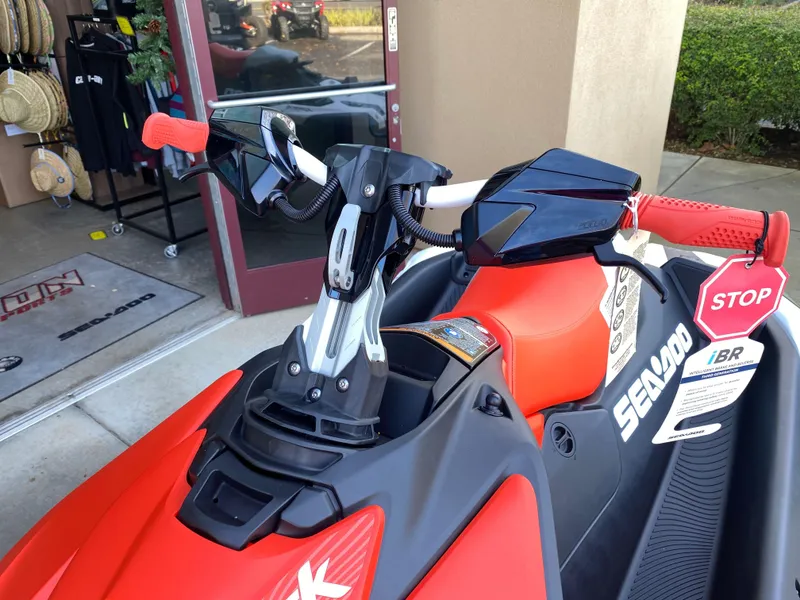 Slide: The Image of 2024 Sea-Doo Spark Trixx for 1, vibrant red handlebars, displayed in showroom. - 2