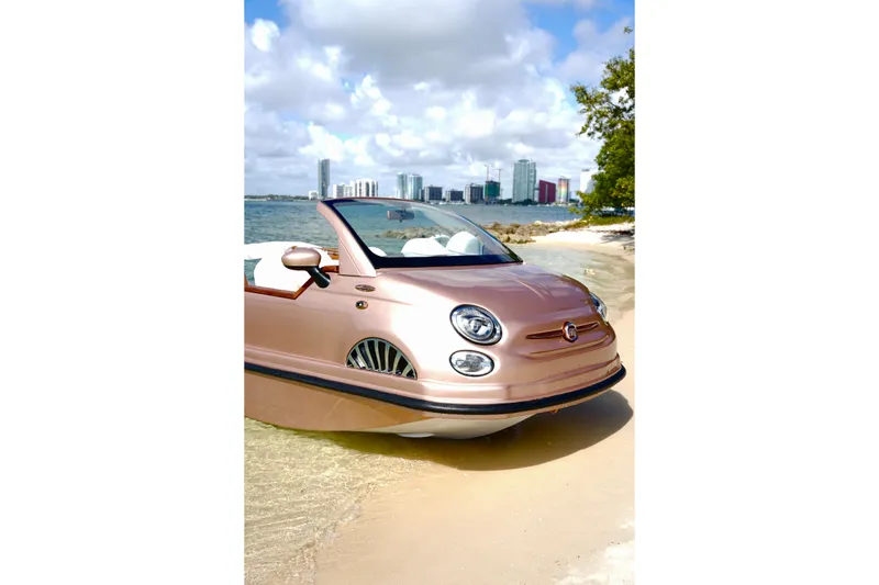 Slide: The Image of Rose Gold Fiat 500 boat on sandy beach, city skyline in background, 2026 model. - 23
