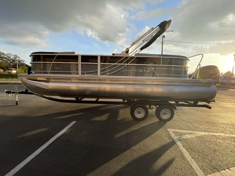 Slide: The Image of 2025 South Bay S224RS pontoon boat on trailer, parked under a cloudy sky. - 33
