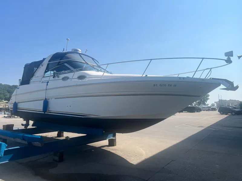 The Image of 1998 Sea Ray 290 Sundancer boat on a trailer in a sunny marina. - 0