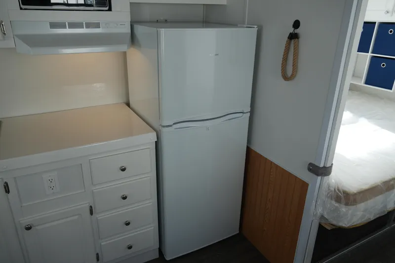 Slide: The Image of 2024 Catamaran Aqua Lodge kitchen with white fridge, cabinets, and adjacent bedroom. - 17