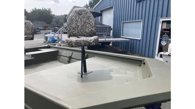 Slide: The Image of 2025 Lowe Roughneck RX1660 Tiller boat with camo seat, parked outside a blue building. - 4