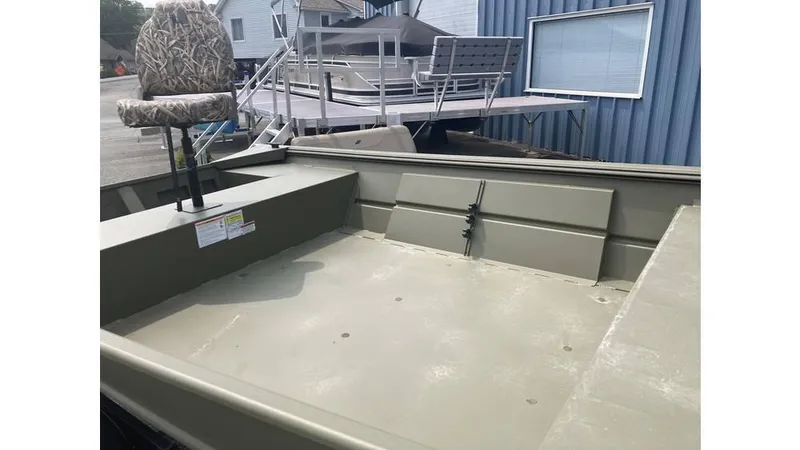 Slide: The Image of 2025 Lowe Roughneck RX1660 Tiller boat interior with camo seat, docked near blue building. - 5